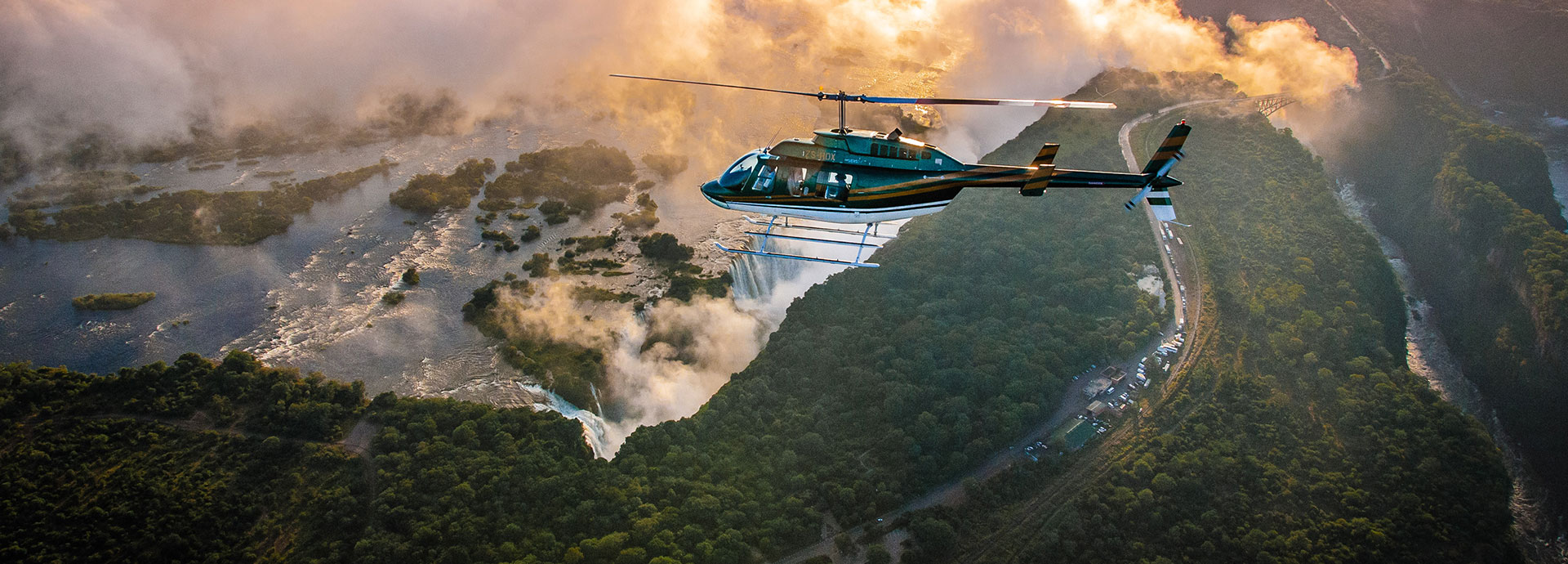 A helicopter flies over the majestic mists of Victoria Falls at sunset
