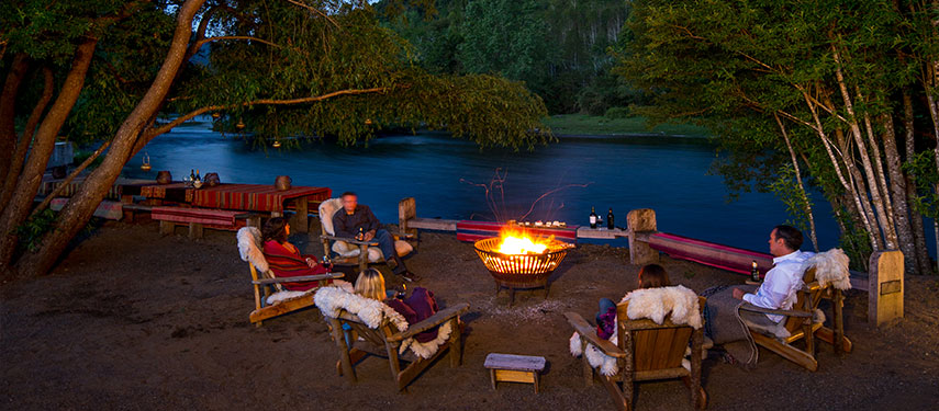Guests gathered around an outdoor fire on the banks of Liucura River in Chile's Lake District