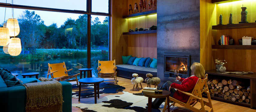 Woman sitting in front of a roaring open fire in the lounge room of Hotel Vira Vira in Patagonia, Chile
