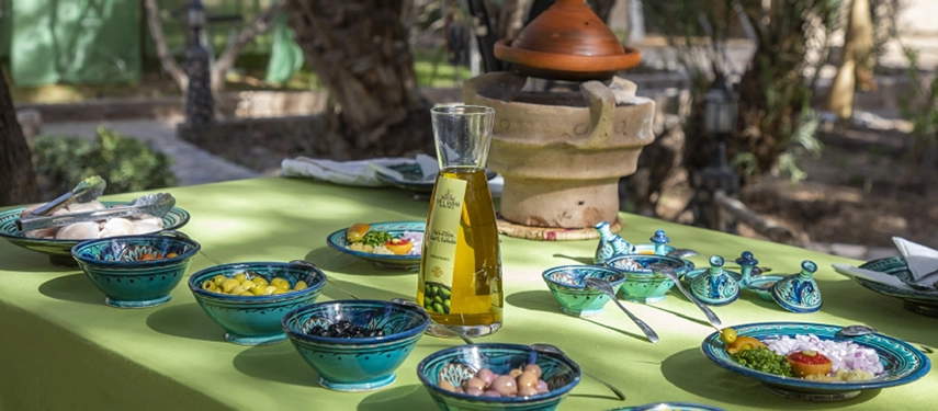 Colourful Moroccan table setting with olive oil, tagine, and bowls of fresh ingredients for a traditional meal.